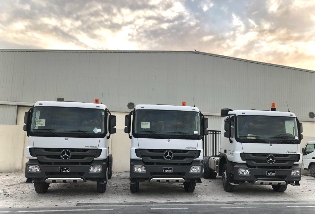 Three white tipper tractor units lined up outside a steel warehouse